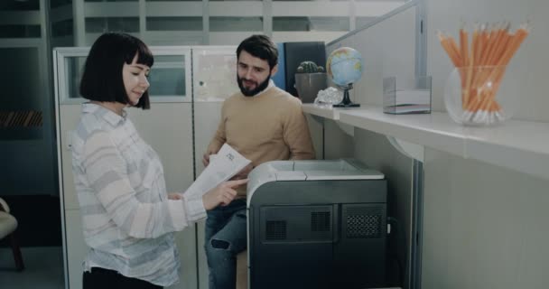 I office flickan skriva ut några dokument och tala med hennes kollega. — Stockvideo