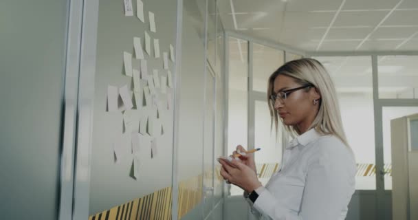 Στο γραφείο, εργαζόμενος γυναίκα και άνδρες κάνει κάποιο σχέδιο εργασίας και να κολλήσει σημειώσεις στον τοίχο του γραφείου του — Αρχείο Βίντεο