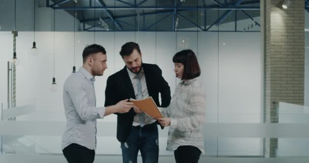 Tres socios de negocios hablando en el corredor en el centro de negocios acerca de un proyecto, mirando en el mapa — Vídeos de Stock