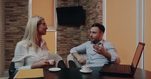 Két irodai dolgozó van egy szép beszélgetés az üzleti központ kávézójában, az asztalnál — Stock videók