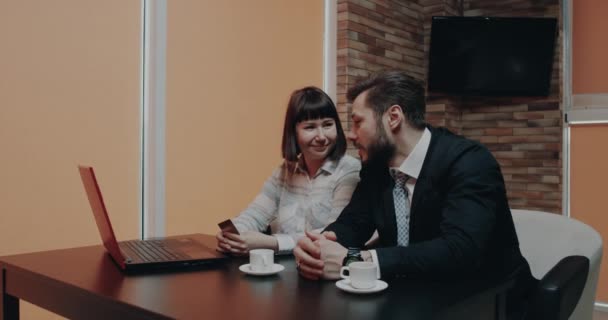 Mladí muži učení jeho kolega objednal něco od notebooku pomocí karty jsou spokojení a usměvaví — Stock video