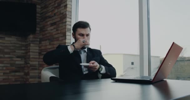 Jeune entreprise avec un visage sérieux prenant son café à la pause et en regardant à travers l'ordinateur portable — Video