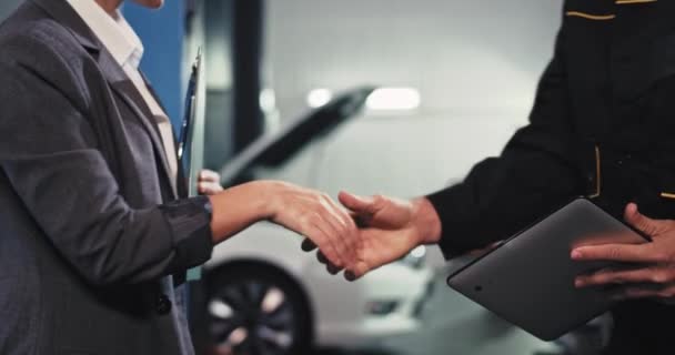 Señora guapa en un traje estrechando la mano con un mecánico de automóviles delante de la cámara hacen un trato y luego van delante del coche para analizar el problema — Vídeo de stock