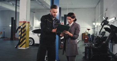 Olgun tamirci ve çekici bayan araba garajındaki sorunu kontrol etmek için arabaya gitmeden önce bazı evrakları imzalarlar.