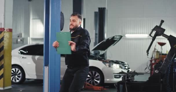 在汽车维修部门跳舞的机械师拿着地图，他很兴奋，这很划算 — 图库视频影像