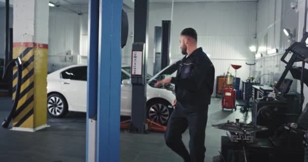 Devant le mécanicien de la caméra dans un service moderne auto vérifier la voiture et danser excité au travail, il profite de la journée — Video