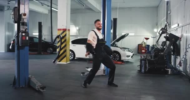 Vicces és izgatott szerelő férfi táncol a kamera előtt egy tágas szolgáltatás auto center — Stock videók