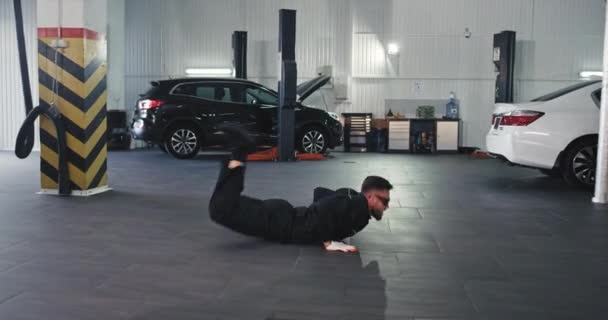 Mycket upphetsad modern mekaniker kille dansar det n och flytta karismatisk framför kameran i en rymlig och modern service auto center — Stockvideo