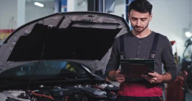 Mükemmel görünümlü tamirci elinde bir liste ile kameraya bakıyor ve gülümsüyor.