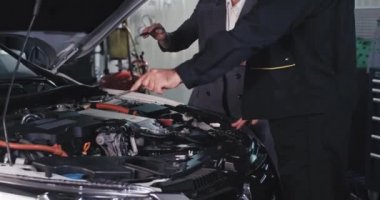 Takım elbiseli güzel bir iş kadını garajda tamirciyle sohbet ediyor arabanın başında dikiliyor ve sorunu analiz ediyor.