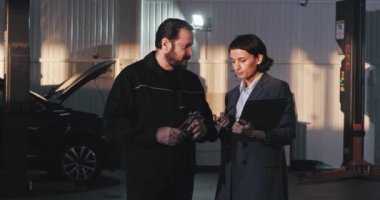Office manager woman in a suit have a conversation with a service auto worker in the garage they analyzing the plan of work