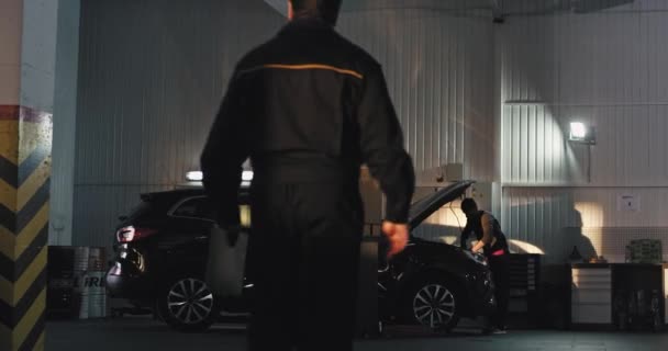 Moderne auto service center belangrijkste monteur in een uniform gaat naar de andere monteur man om het probleem van de auto te vinden — Stockvideo