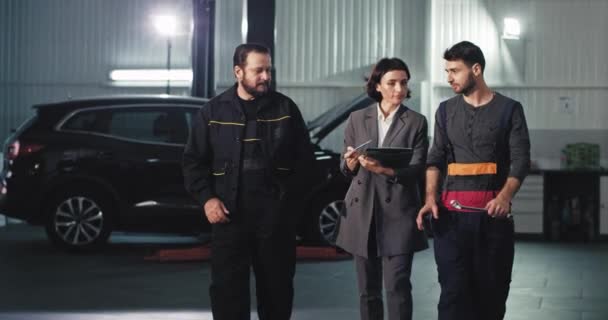 Przed kamerą auto serwis zespół kobieta główny menedżer i dwóch mechanik analizując plan pracy skoncentrowany mają rozmowę — Wideo stockowe