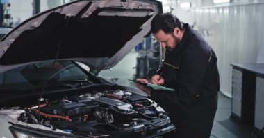 Tamirci üniformalı adam arabanın sorununu modern servis merkezindeki bir haritaya yazmış.
