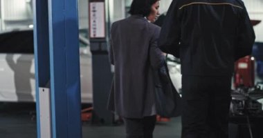 Güzel bir kadın takım elbiseli ve servis otomobili ile arabanın üzerinde tamirciyle konuşuyor.