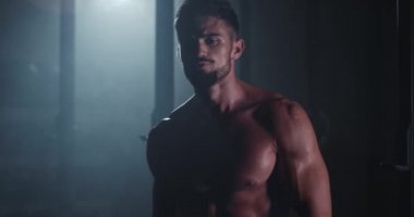 Çekici vücut geliştirme elemanı koyu renk spor sınıfında kameraya doğru yürüyor.