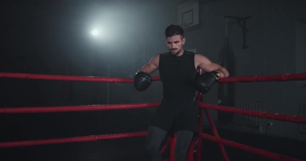 Un tipo guapo en un ring de boxeo tiene un descanso entre su combate de boxeo, tiene un entrenamiento intenso — Vídeos de Stock