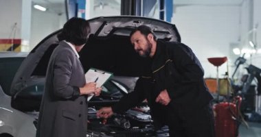 Servis arabalı müşteri bayan tamirciyle sohbet ediyor. Arabanın neresini tamir edeceklerini görmek için bakıyorlar.