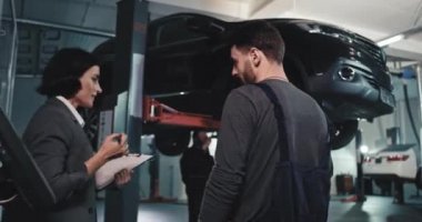Takım elbiseli güzel bir kadın ana tamirci ve diğer olgun tamirciyle iş planını analiz eden hasarlı araba hakkında konuşuyor.