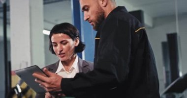 Araba tamirhanesinde iş konsepti. Araba sahibi kadın. Tamirciyle arabasının sorununu analiz ediyor.