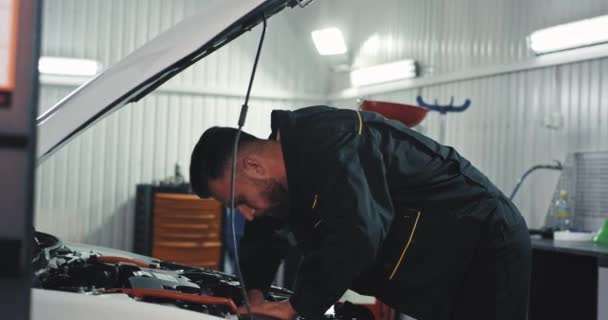 Mekaniker ung kille i uniform koncentrerad arbetar på en bil fixa problemet han får svettas — Stockvideo