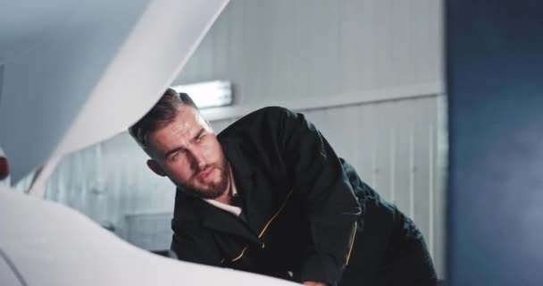 Attractive guy portrait in front of the camera mechanic in a service auto working concentrated fixing the car engine and get sweating — Stock Video