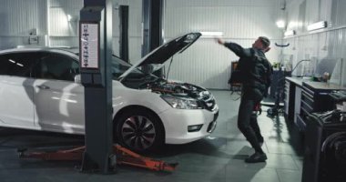 Çekici bir tamirci. Üniformalı. Kameranın önünde dans ederken arabanın üzerinde çalışıyor.