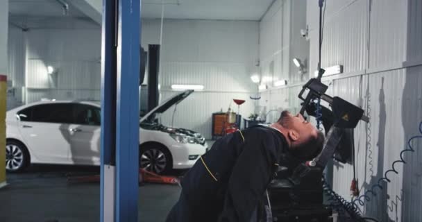 En un auto moderno servicio de buen aspecto chico mecánico en un uniforme bailando feliz mientras se comprueba la fijación del coche — Vídeos de Stock