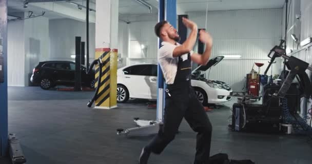 Moderno garage auto giovane meccanico danza eccitato all'allenamento durante il fissaggio della macchina, ha un buon umore e grande giornata di lavoro — Video Stock