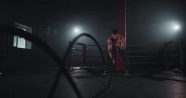 Modern bir vücut geliştirme sınıfında halatlarla egzersiz yapan adam kameranın önünde çok sıkı çalışır.