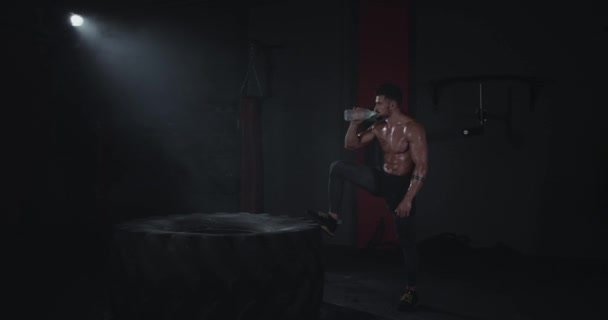 Forte uomo muscolare bere acqua assetata da una bottiglia di plastica dopo l'allenamento in una classe di fitness croce — Video Stock