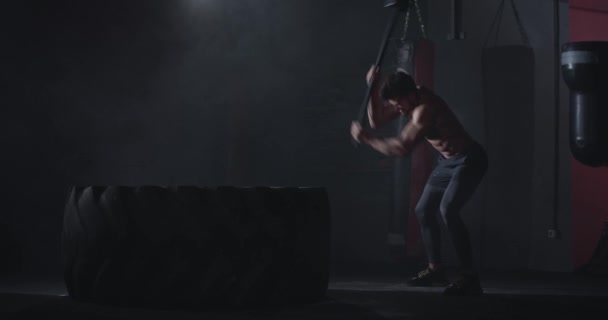 Харизматичный сильный мускулистый атлетик имеет Хаммер упражнения над большой шиной, делая его крест фитнес тренировки в тренажерном зале — стоковое видео