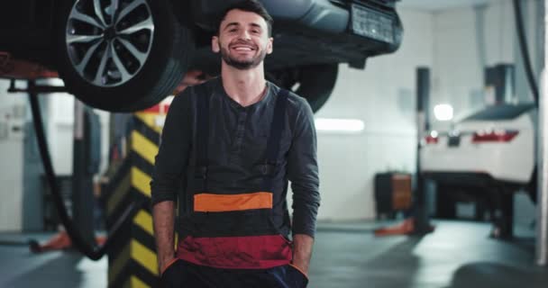 Bello sguardo giovane meccanico in uniforme guardando dritto alla fotocamera sorridente grandi e mani incrociate in un moderno garage auto — Video Stock