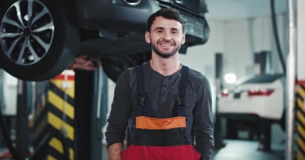 Glad mekaniker arbetare från en auto servicecenter framför kameran tittar rakt leende och njuta av tiden på sin arbetsplats — Stockvideo