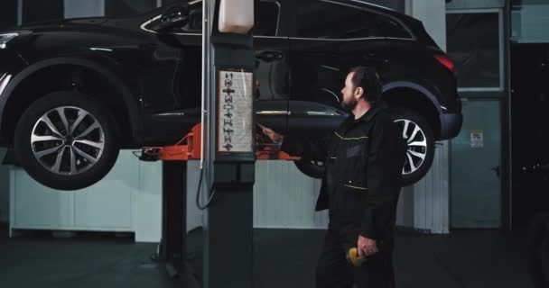 Hombre mecánico de coche maduro bajar el coche después de que terminó de arreglar la suspensión del coche en un moderno centro de servicio automático — Vídeos de Stock