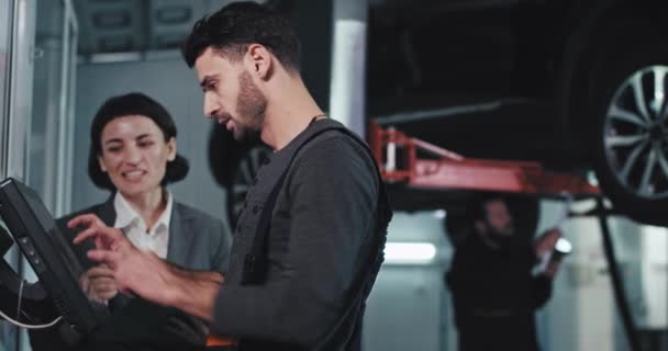 Car service concept good team car mechanic guy have a friendly conversation with the owner lady of the damaged car while make some notes on his work computer — Stock Video