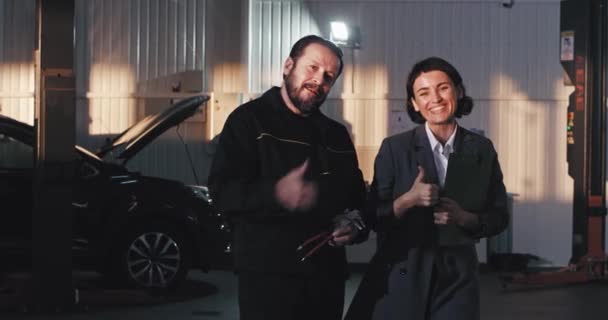 Mature mechanic man and his supervisor lady in a suit smiling large in front of the camera showing big like happy in a auto service center — Stock Video