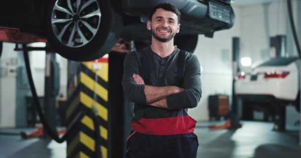 In the auto garage mechanic guy in the uniform in front of the camera with a large smile and good mood looking straight to the camera — Stock Video
