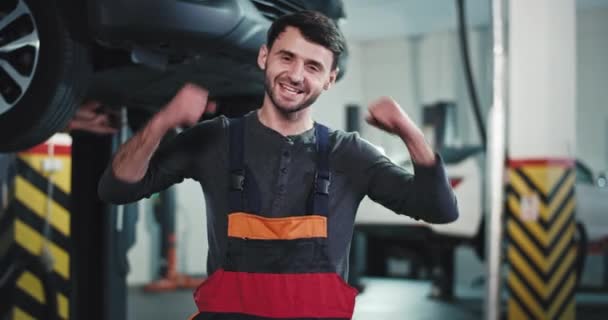 Aufgeregter Kfz-Mechaniker im Autoservice-Center vor der Kamera, freut er sich, nachdem er das beschädigte Auto repariert hat — Stockvideo