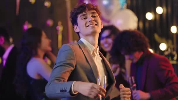 Retrato de un joven guapo con un traje casual bailando delante de la cámara en la fiesta disfrutando de la noche sosteniendo una copa de vino espumoso. Disparo en ARRI Alexa Mini — Vídeo de stock