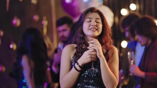 Úžasná hezká dáma s dlouhými kudrnatými vlasy a velkým úsměvem před kamerou, která si vychutnává atmosféru večírku se sklenicí šampaňského — Stock video