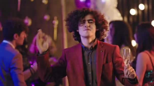 Attraktiv och karismatisk ung man i en avslappnad kostym som håller ett glas champagne framför kameran och dansar roligt på stor fest — Stockvideo