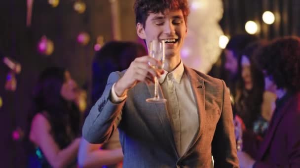 Good looking young guy in a casual suit enjoying the evening at party drinking some sparkling wine background big party atmosphere. — Stock Video