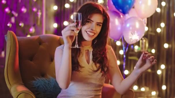 Bella signora con un grande sorriso alla festa di Natale, tenendo scintilla e un bicchiere di champagne godendo il momento sul divano. 4k — Video Stock