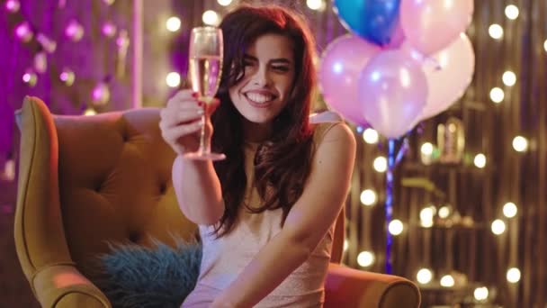 Ritratto di una signora carismatica con un grande sorriso sul divano alla festa di compleanno guarda dritto alla macchina fotografica e beve un po 'di champagne — Video Stock