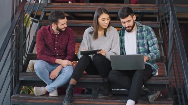 Primo piano tre studenti della biblioteca fanno un progetto insieme utilizzando un tablet elettronico e un notebook — Video Stock