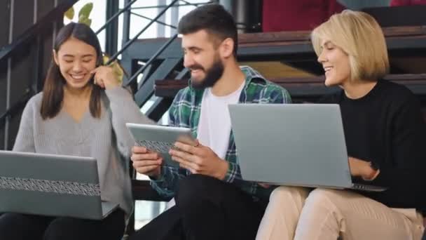 Em um moderno centro de escritórios com um trabalhador multiétnico no estreito, eles têm tablet e notebook trabalhando relaxados e aproveitando o tempo em seu local de trabalho — Vídeo de Stock