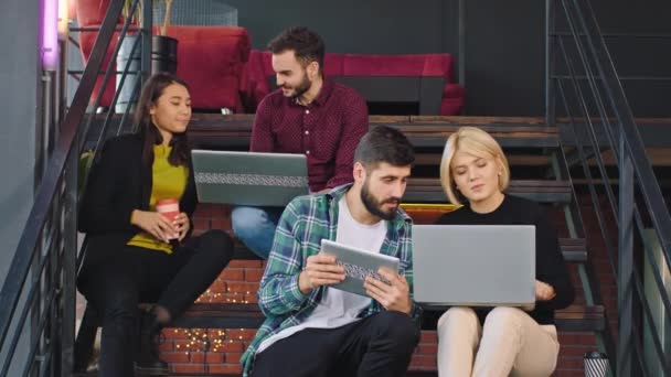 Attraktive multiethnische Studenten, die ihre Hausaufgaben in der Bibliothek machen und alles analysieren, während sie Tablet und Notizbuch benutzen — Stockvideo