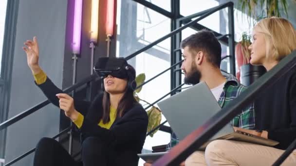 Travailleur de bureau multiethnique pendant une pause café en utilisant les lunettes de réalité virtuelle pour jouer à un jeu virtuel tout en étant assis sur les escaliers du bureau. Tourné sur ARRI Cinema Camera — Video