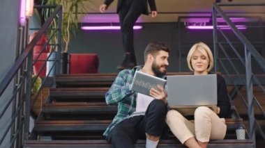 Ofis merdivenlerinde çok ırklı genç işçiler sohbet ettikleri ve iş yerlerinde kendilerini harika hissettikleri bir not defteri kullanarak çalışma planını analiz ediyorlar..